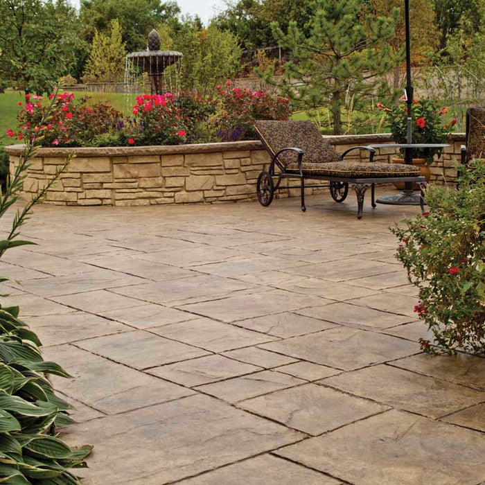 a freshly sealed brown/red concrete porch surrounded by potted plants. On the porch is concrete outdoor fountain made to look like stone. There are pink-red flowers along the border of the fountain