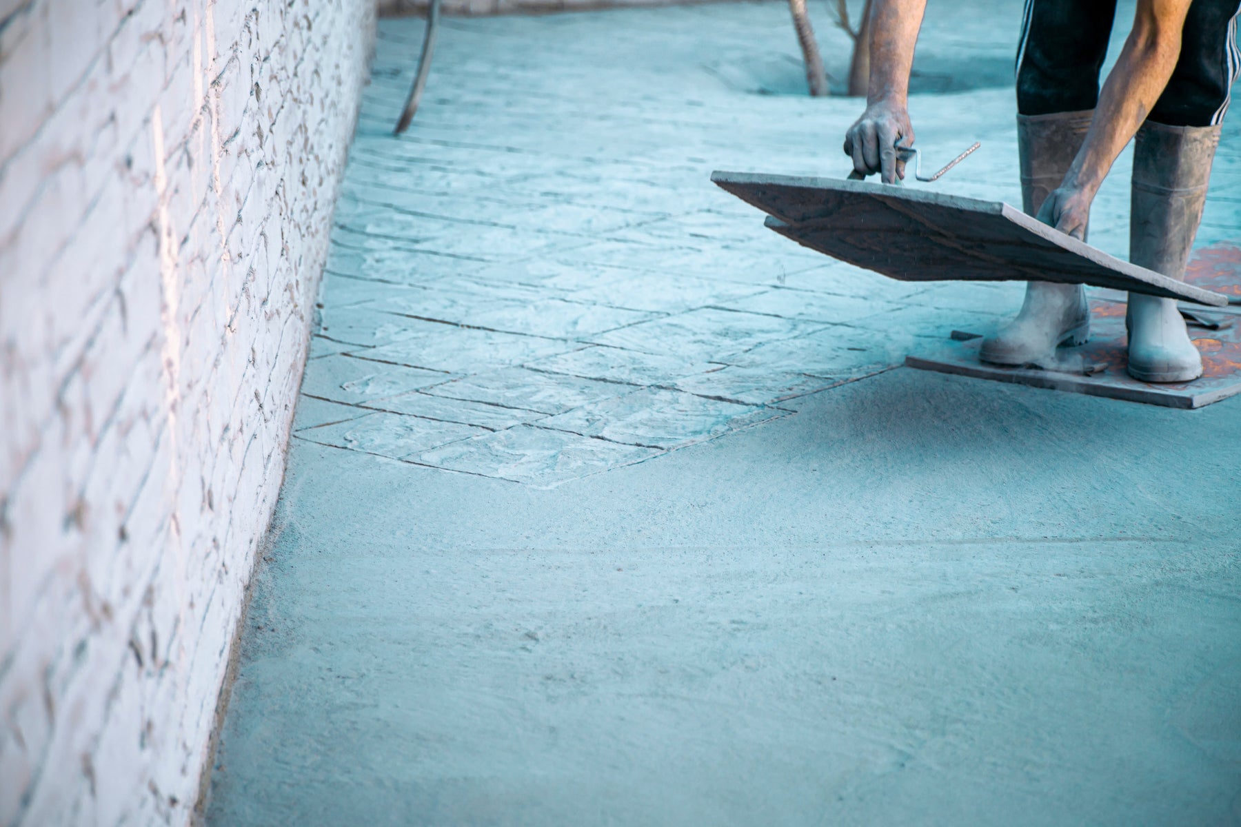 A person is standing on a concrete mat and in the process of placing another one. The concrete being stamped is blue.