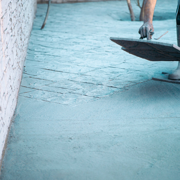 A person is standing on a concrete mat and in the process of placing another one. The concrete being stamped is blue.